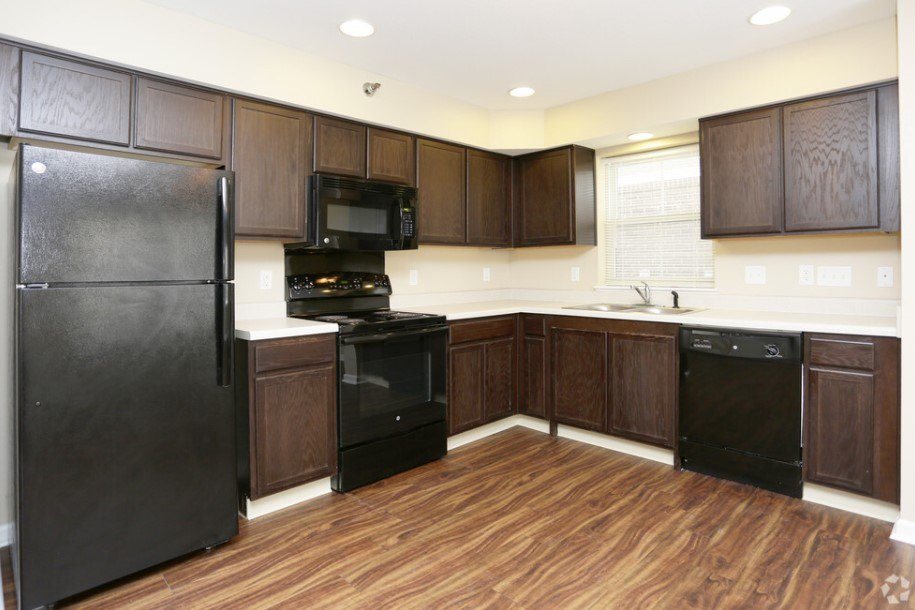 A black refrigerator is in a kitchen with wooden cabinets.